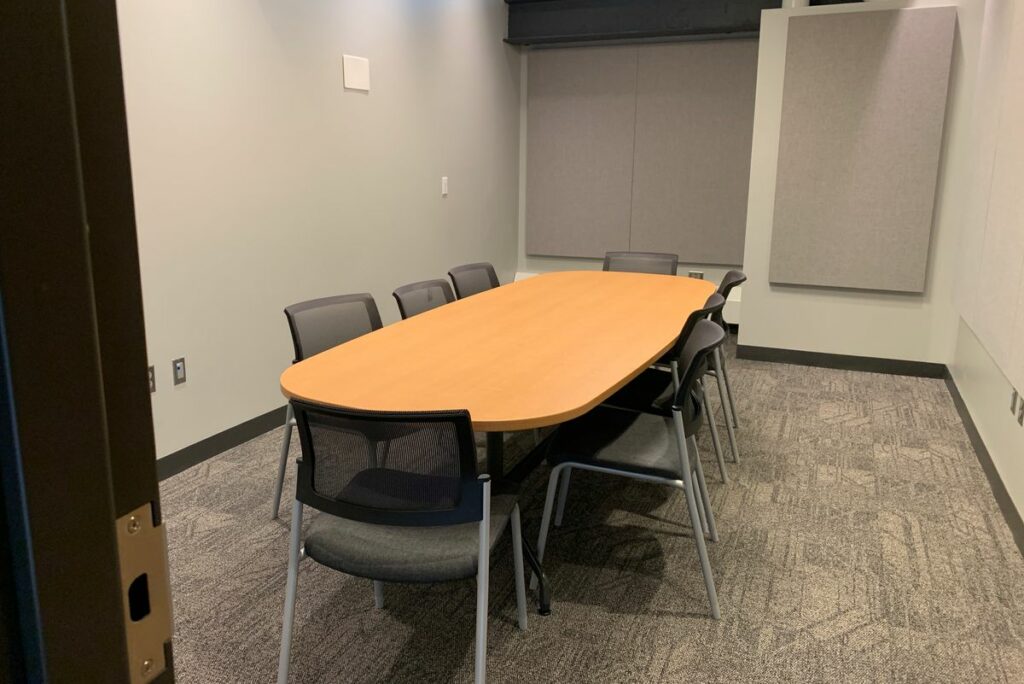 A meeting room with a large oval table in the middle surrounded by office chairs.