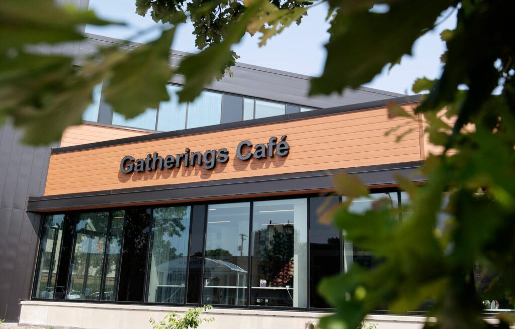 A front of a building with large glass windows. A sign reads Gatherings Cafe.