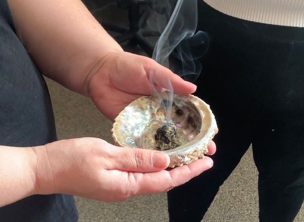 A woman holds an abalone shell filled with sacred medicines and smudges.