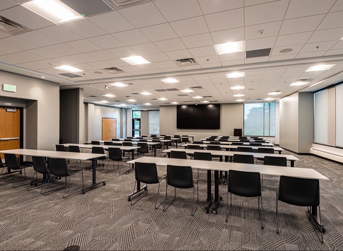 A conference room with long tables and chairs. There's a large screen at the front of the room.