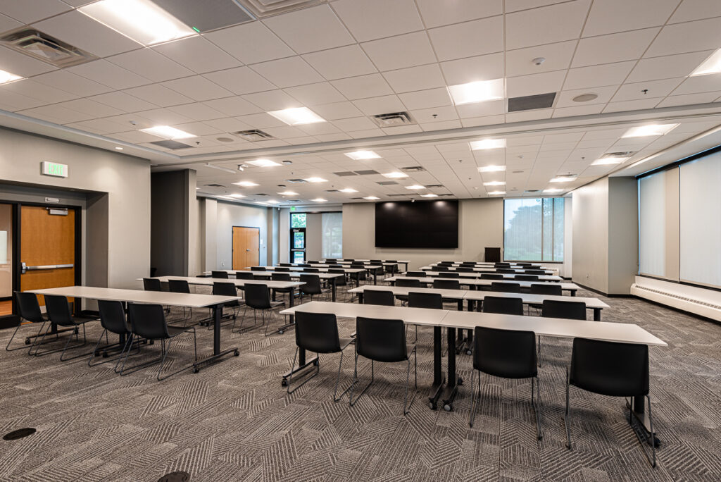 A conference room with long rectangular classroom style tables and a large presentation screen.